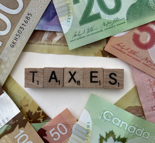 Wooden tiles spelling “taxes” are surrounded by Canadian cash