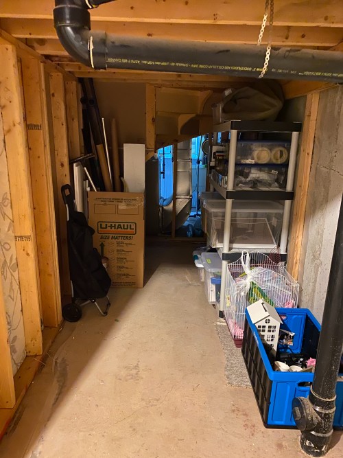 a futon, a mattress, a blanket and other items are stored in a narrow space in the basement