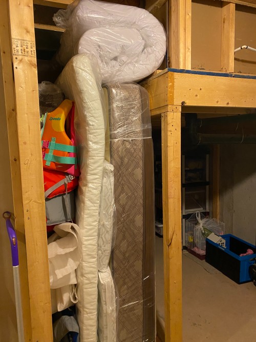 a futon, a mattress, a blanket and other items are stored in a narrow space in the basement