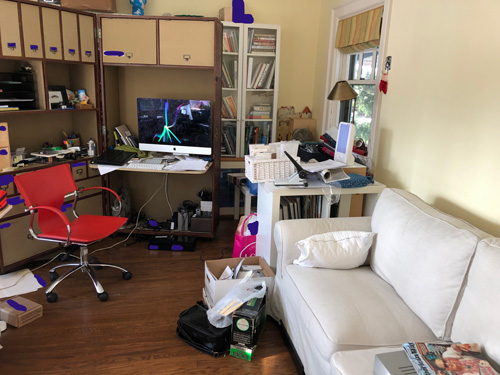 a desk, couch and bookshelf in a room with lots of stuff everywhere