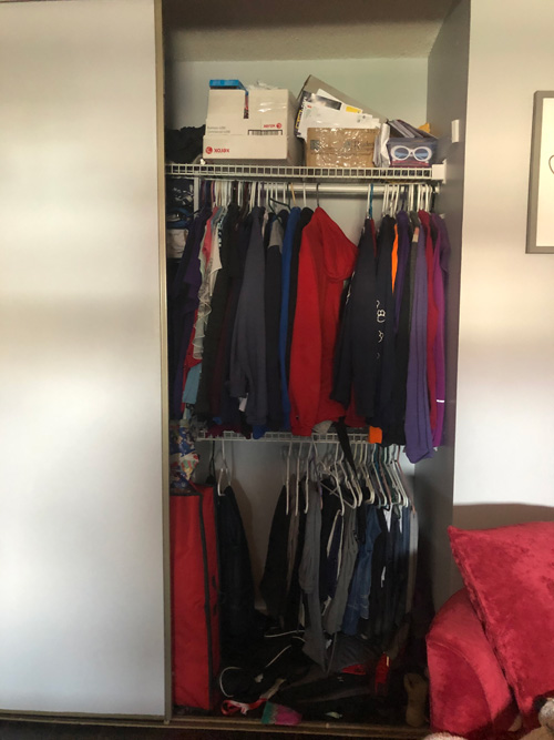 closet with sliding door filled with clothes and boxes