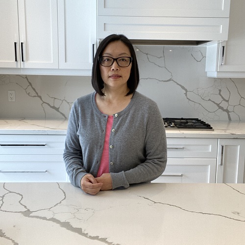 Female standing behind the kitchen counter looking into the camera.