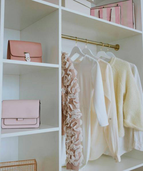 Shelving in closet with pink purses, cream and beige clothing